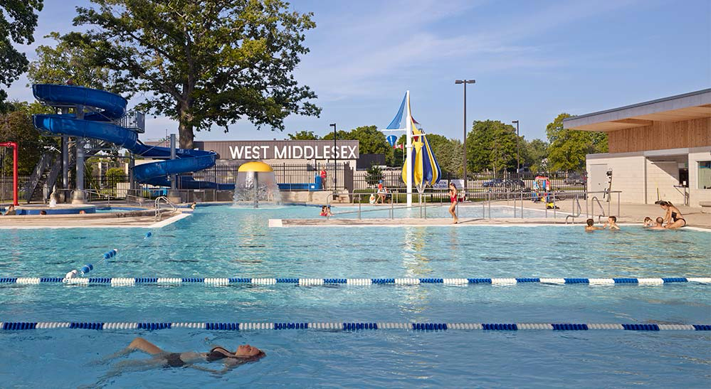 Outdoor lap/leisure pool with water slide, water umbrella, and dumping buckets at Fairgrounds Aqua Park in Strathroy, Ontario